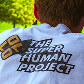 Man wearing a white shirt with "The Super Human Project" printed on the back.